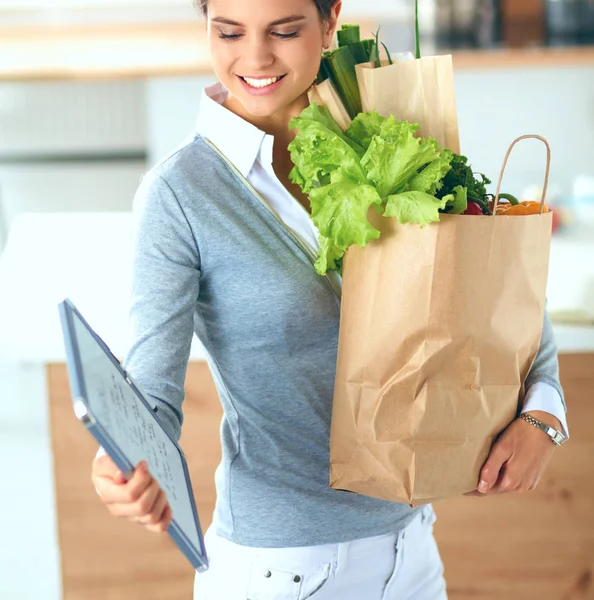 Egy fiatal nő zöldséges bevásárlószatyrot tart a kezében. A konyhában állok. — Stock Fotó