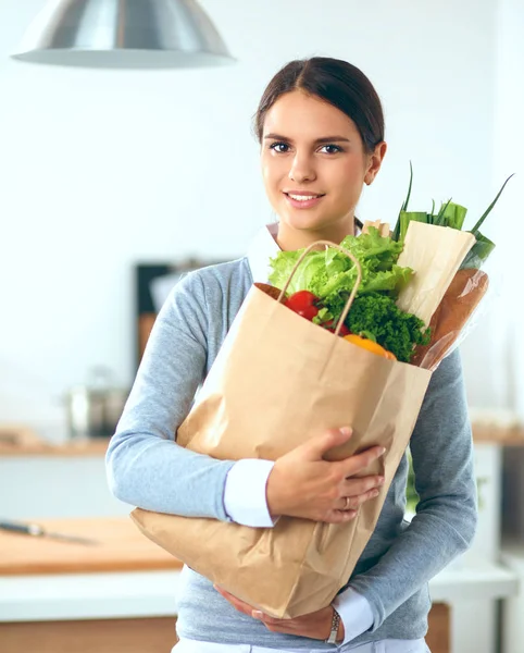 Wanita muda memegang tas belanja dengan sayuran. Berdiri di dapur — Stok Foto