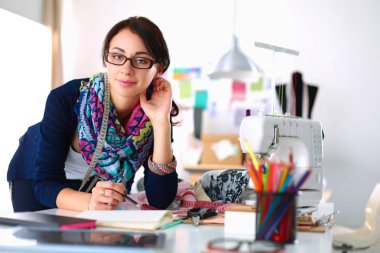 Güzel moda tasarımcısı stüdyoda masada oturuyor.