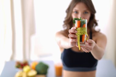 Elinde bardak dolusu taze meyve salatası ve bardağın etrafında mezura tutan bir kadın.