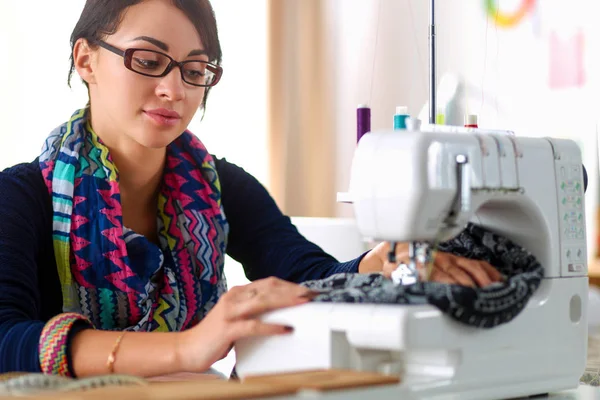 Junge Frau näht, während sie am Arbeitsplatz sitzt — Stockfoto