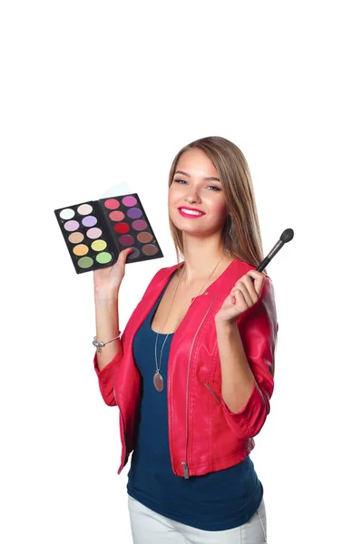 Ung vacker kvinna håller i ena handen och en palett med färg och skuggor för makeup, begagnad pensel för makeup — Stockfoto