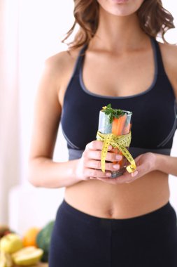 Elinde bardak dolusu taze meyve salatası ve bardağın etrafında mezura tutan bir kadın.