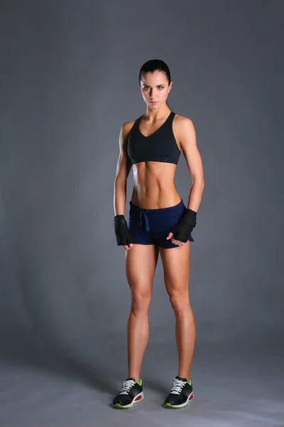 М'язиста молода жінка позує в спортивному одязі на чорному тлі — стокове фото