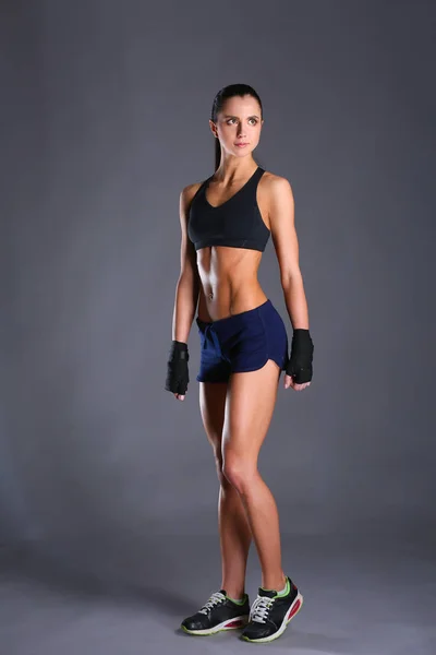 Muscolare giovane donna in posa in abbigliamento sportivo contro sfondo nero — Foto Stock