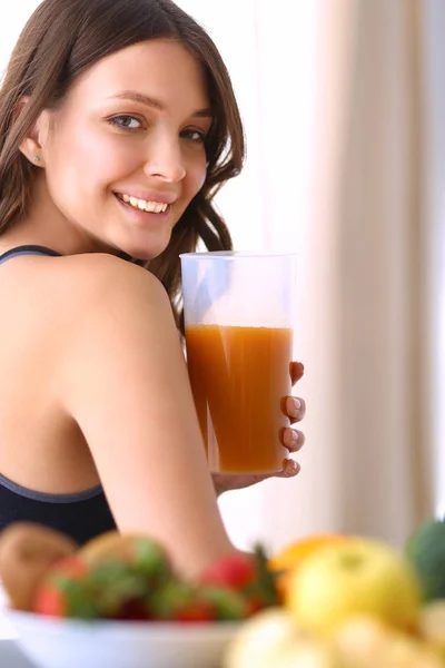 Menina sentada na cozinha na mesa com suco de frutas e copos — Fotografia de Stock