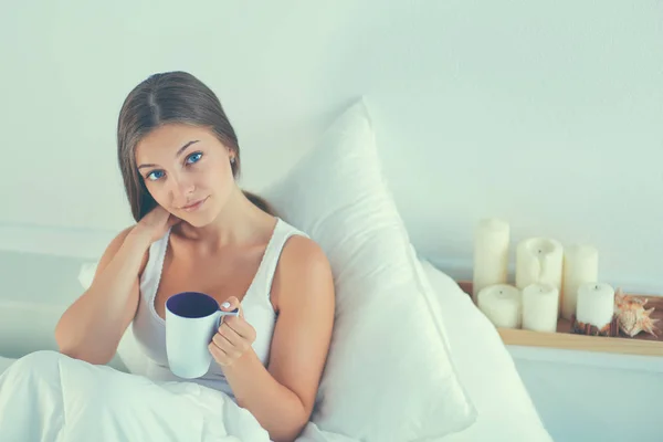 Mujer joven y bonita en la cama disfrutando de una taza de té — Foto de Stock