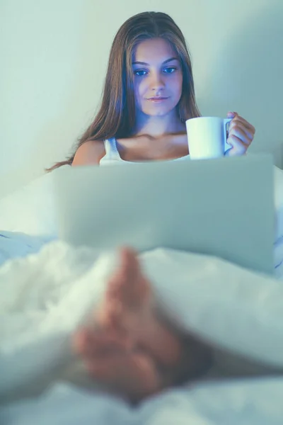 Dość młoda kobieta z laptopa w łóżku i cieszyć się filiżanką herbaty — Zdjęcie stockowe
