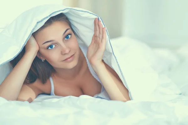 Joven hermosa mujer acostada en la cama bajo cubierta — Foto de Stock