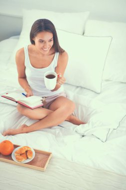 Yatakta oturmuş ve bir defterini yazma genç güzel kadın