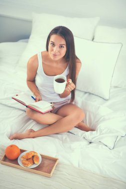 Yatakta oturmuş ve bir defterini yazma genç güzel kadın