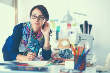 Güzel moda tasarımcısı stüdyoda masada oturuyor.