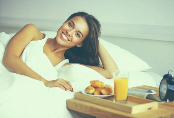 Schöne junge Frau sitzt im Bett und frühstückt — Stockfoto