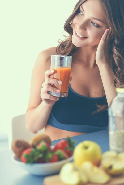 Menina sentada na cozinha na mesa com suco de frutas e copos — Fotografia de Stock