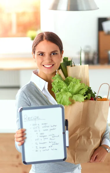 Giovane donna che tiene la borsa della spesa con verdure. In piedi in cucina — Foto Stock