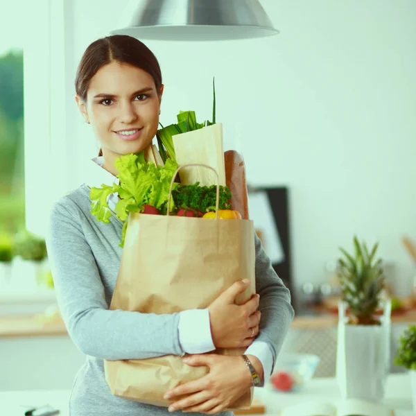Jonge vrouw met boodschappentas met groenten Staande in de keuken. — Stockfoto