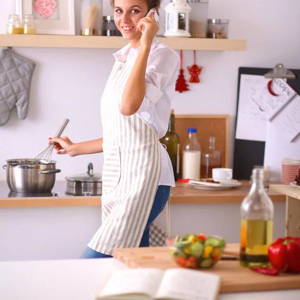 描绘一个微笑的女人，家里厨房里有电话 — 图库照片
