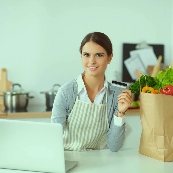 Lachende vrouw online winkelen met behulp van computer en creditcard in de keuken — Stockfoto