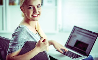 Genç ve güzel bir kadın evde dizüstü bilgisayar kullanıyor.