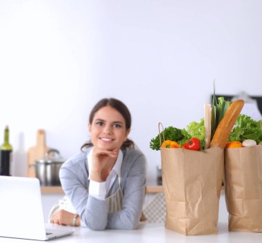 Güzel genç bayan yemek pişiriyor. Mutfakta makbuzu olan dizüstü bilgisayara bakıyor.