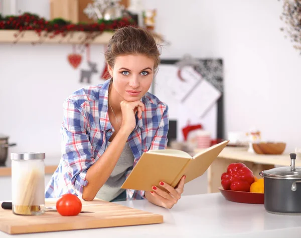 Jovem mulher lendo livro de receitas na cozinha, à procura de receita — Fotografia de Stock