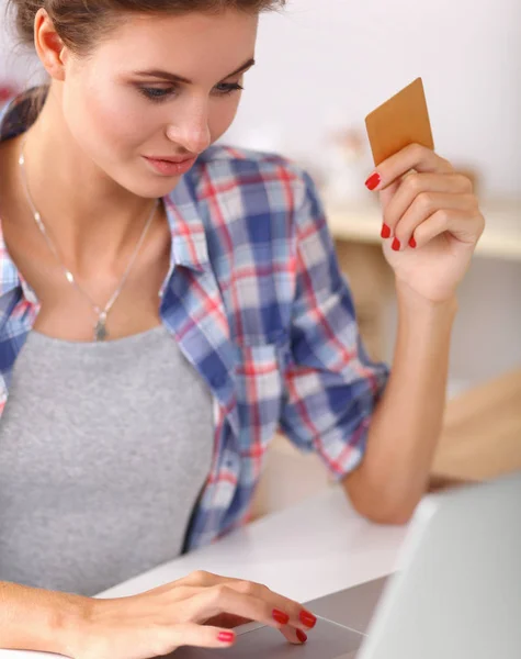 Посміхнена жінка онлайн покупки за допомогою комп'ютера і кредитної картки на кухні — стокове фото