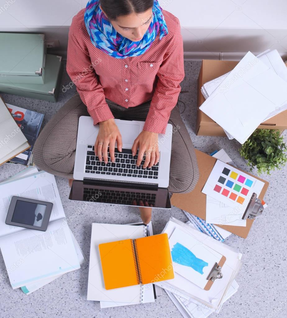 Young attractive female fashion designer working at office desk, drawing while talking on mobile