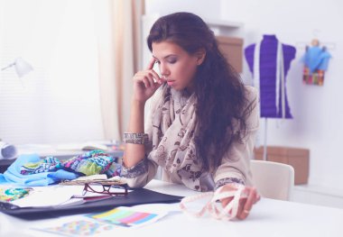 Gülümseyen kadın moda tasarımcısı ofis masasında oturuyor.
