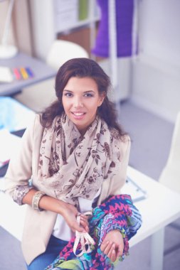 Gülümseyen kadın moda tasarımcısı ofis masasında oturuyor.