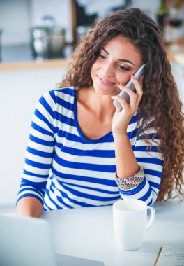 telefonda konuşuyor ve mutfaktaki dizüstü bilgisayar üzerinde çalışan genç güzel kadın portresi