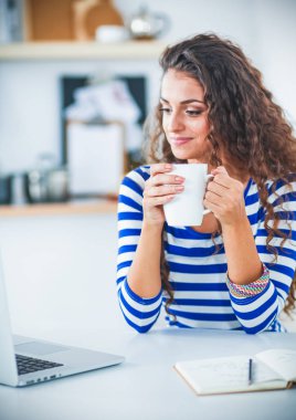 kahve fincanı ve dizüstü evde mutfakta gülümseyen genç kadın