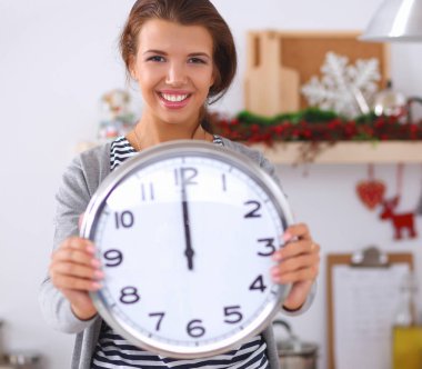 Mutlu genç kadın Noel süslemeli mutfakta saat gösteriyor.