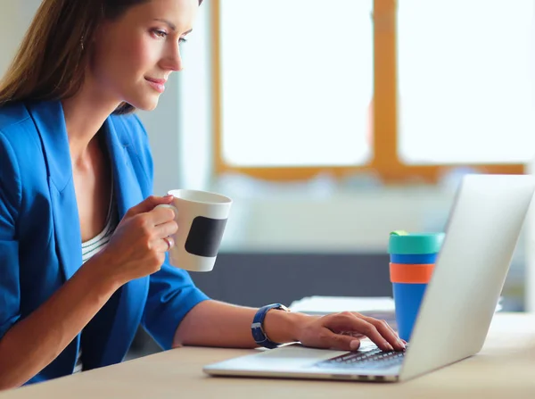 Atractiva mujer de negocios sonriente sentada en el escritorio de la oficina, sosteniendo una taza de café — Foto de Stock