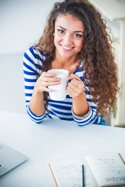 Lachende jonge vrouw met koffiekopje en laptop in de keuken thuis — Stockfoto