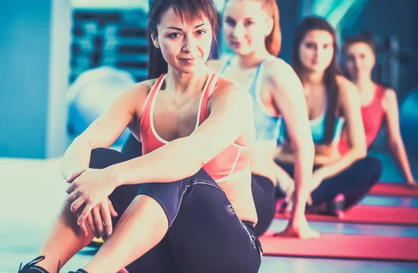 Gente deportiva sentada en colchonetas de ejercicio en un luminoso gimnasio —  Fotos de Stock