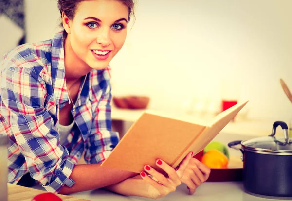 Jonge vrouw die kookboek leest in de keuken, op zoek naar recept — Stockfoto