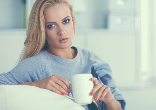Женщина сидит на диване с чашкой в руках — стоковое фото
