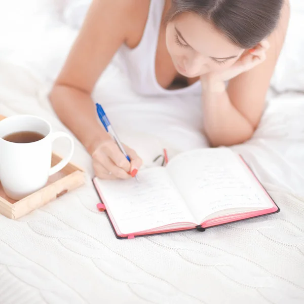 Όμορφη κοπέλα ξαπλωμένη στο κρεβάτι, γράφοντας ένα ημερολόγιο — Φωτογραφία Αρχείου