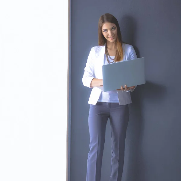 Mujer joven sosteniendo un ordenador portátil, de pie sobre fondo gris — Foto de Stock