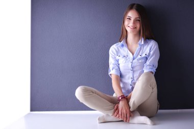 Genç bir kadın yerde, kara duvarın yanında oturuyor.