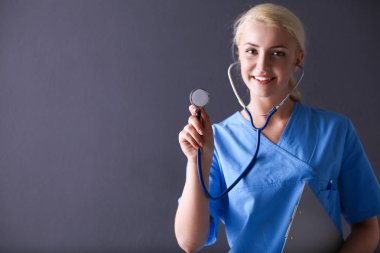 Steteskopla dinleyen kadın doktor, gri arka planda izole edilmiş.