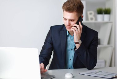Genç işadamı ofiste çalışıyor, masada oturuyor.