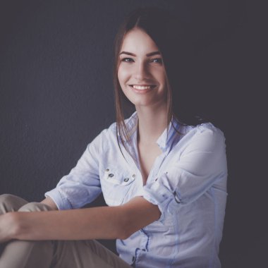 Genç bir kadın yerde, kara duvarın yanında oturuyor.