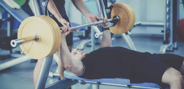 Young man lifting the barbell in gym with instructor — Stock Photo, Image