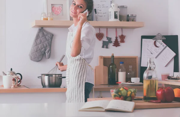 Retrato de una mujer sonriente con teléfono en la cocina en casa — Foto de Stock