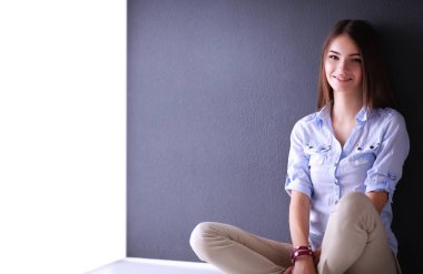 Genç bir kadın yerde, kara duvarın yanında oturuyor.