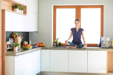 Lotus pozisyonunda mutfak masasında oturan genç güzel kadın