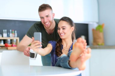 Mutlu çift mutfakta oturmuş smartphone kullanarak