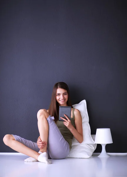 Mujer morena bonita sentada en el suelo con una almohada y mesa de avión — Foto de Stock