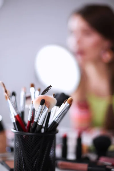 Joven hermosa mujer haciendo maquillaje cerca del espejo, sentado en el escritorio —  Fotos de Stock